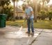 Homeowner pressure washing driveway in sunlight