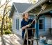 Homeowner removing spider webs from porch eave