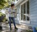 Woman soft washing house exterior on driveway