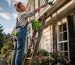 Woman cleaning white gutters outdoors on ladder