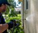 Technician soft-washing stucco from side angle