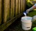 Mixing oxygen bleach beside an algae-stained wood fence